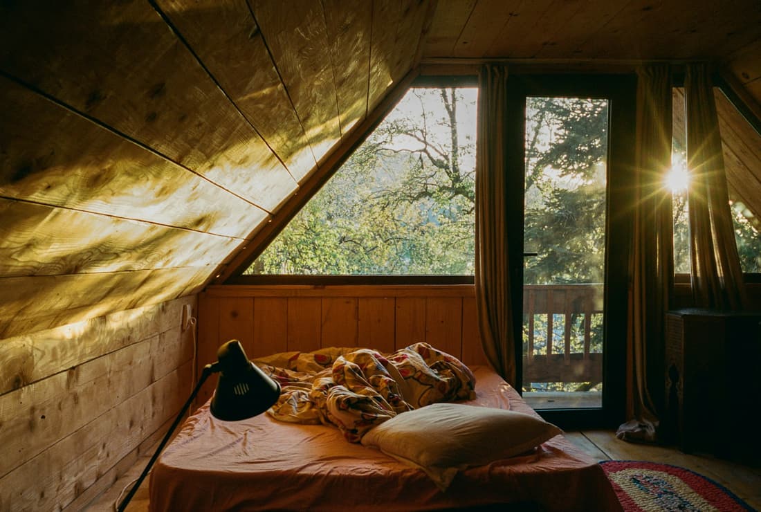 Una camera rivestita in legno nella luce del tardo pomeriggio, con le porte aperte sul balcone.
