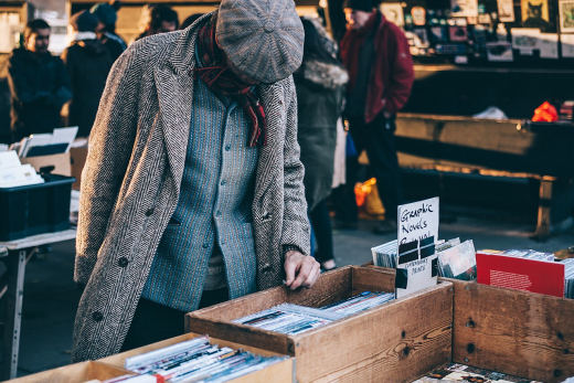 A man in a flat cap browsing boxes of second-hand books at an outdoor stall under Waterloo Bridge.