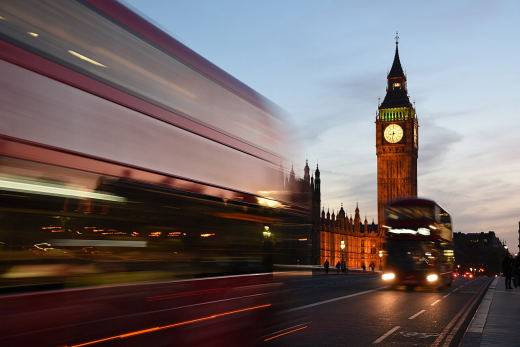 A double decker bus streaking past the Elizabeth Tower in a long exposure at dusk.