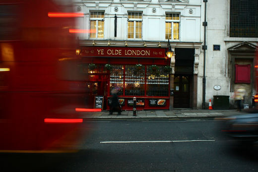 A lit Victorian pub front at night, with a red bus blurring past in the foreground.