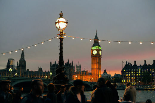 The Houses of Parliament and the Elizabeth Tower at sunset, seen past a lamp post strung with lights.