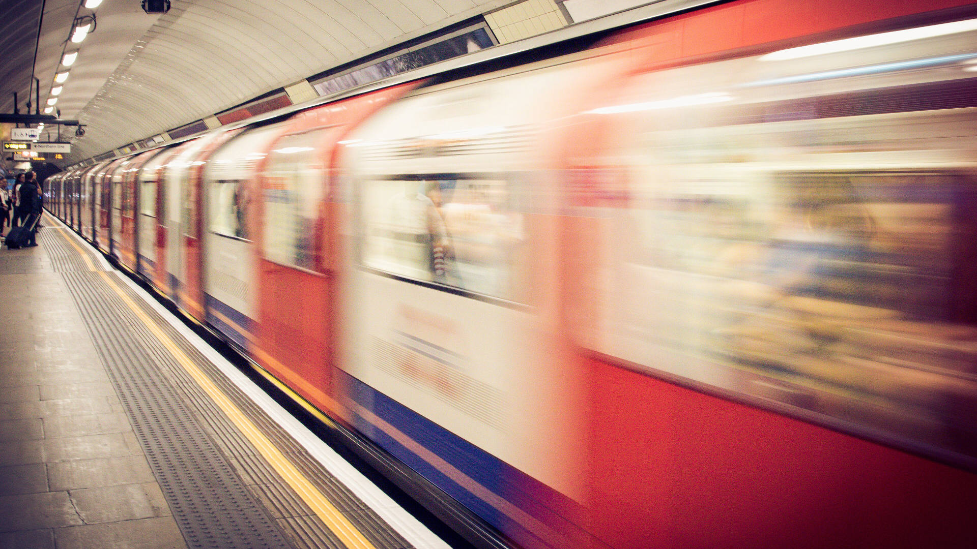 A London Underground train blurred with movement as it passes a platform.
